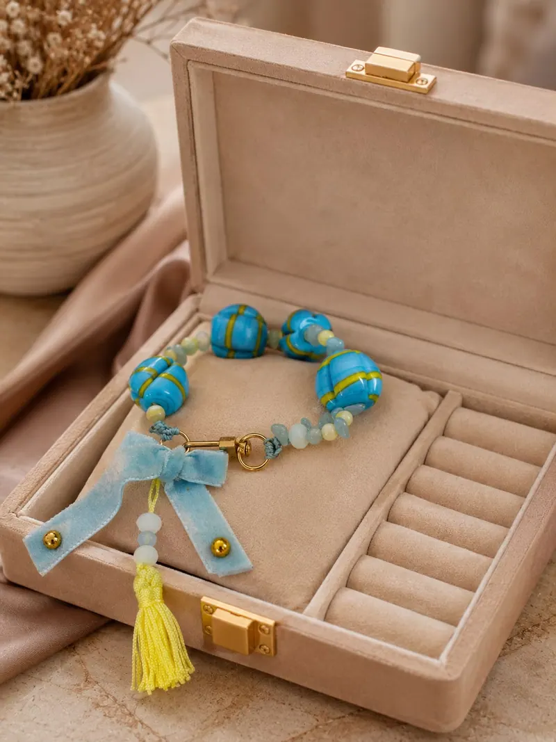 Pulseira de contas turquesa e azuis com laço azul e borla amarela, numa caixa de veludo
